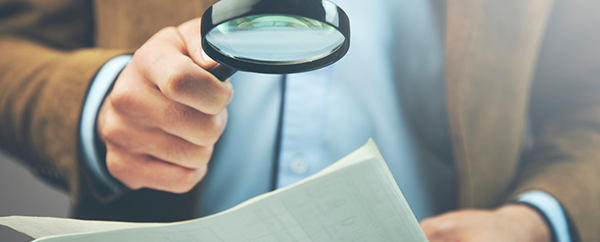 Investigator holding magnifying glass over suspicious document